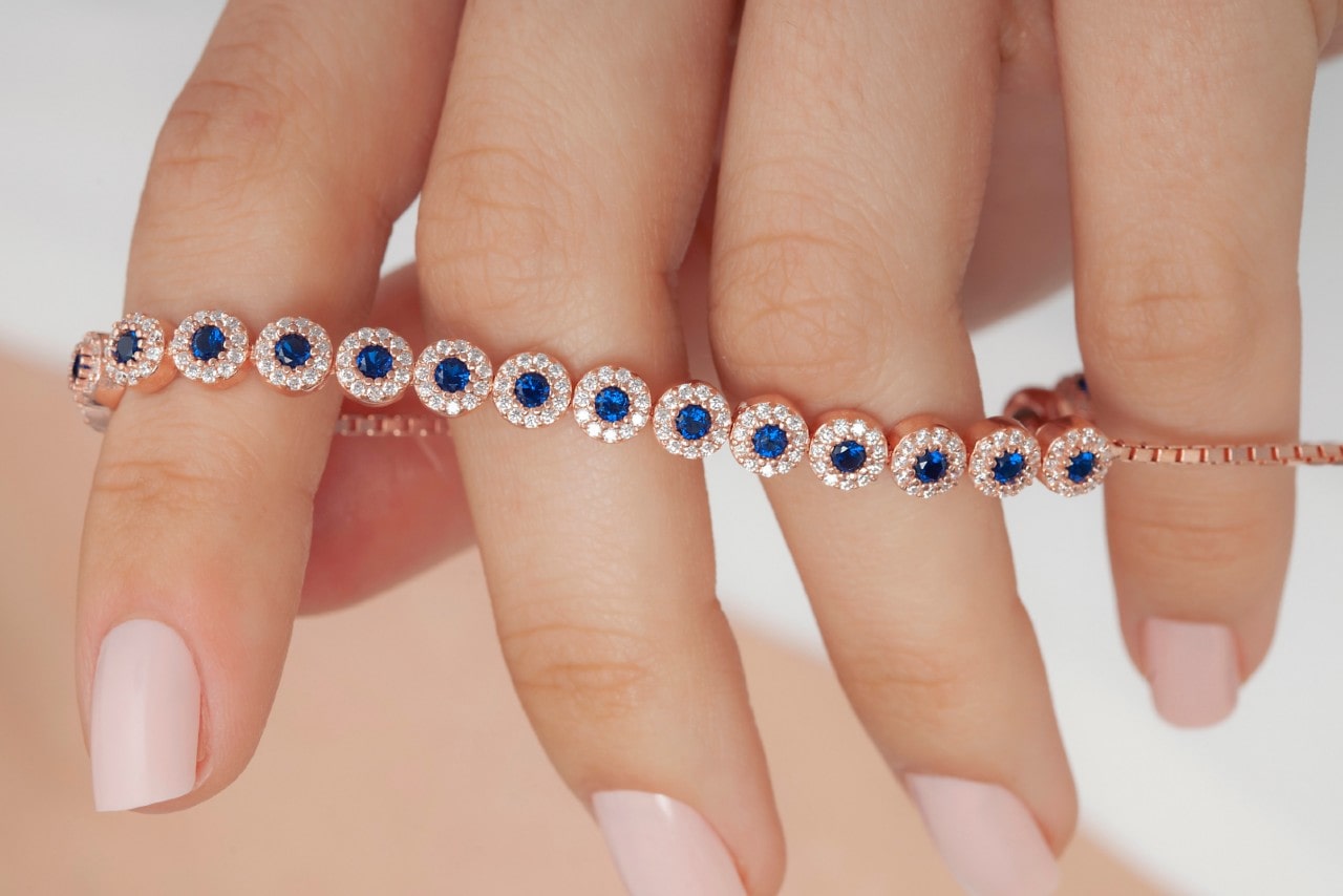 A woman with manicured nails hold a sapphire tennis bracelet.