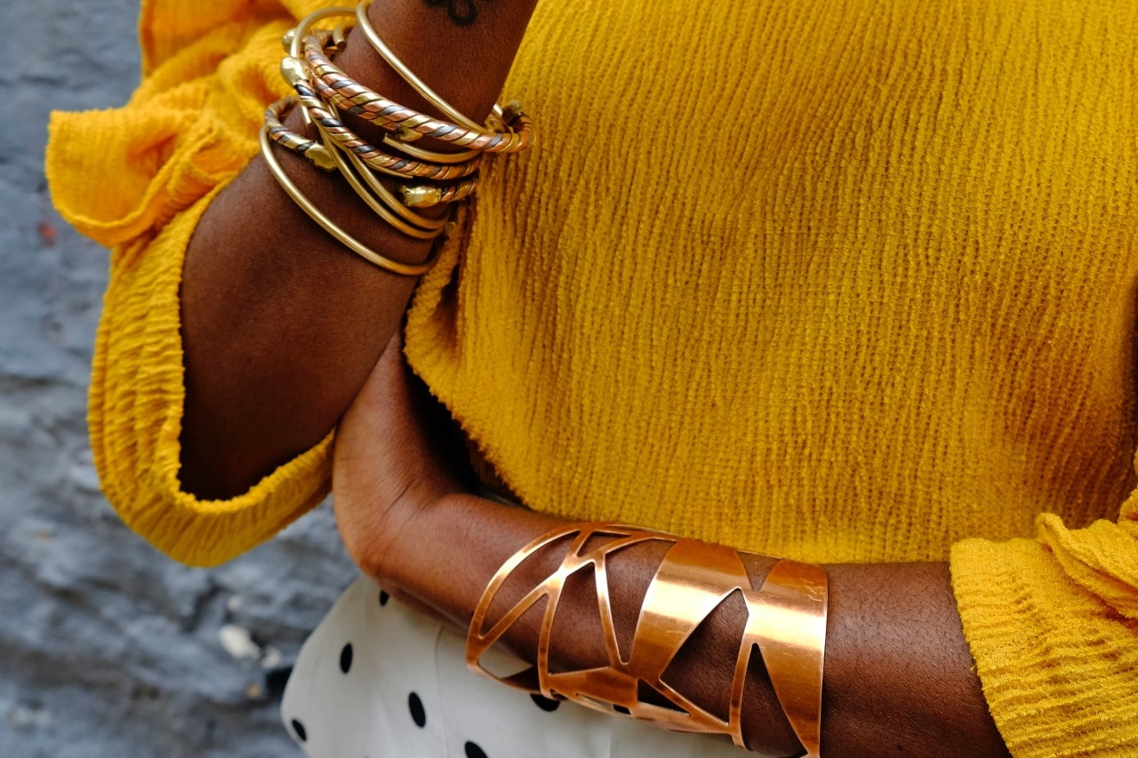 A woman wears a yellow top with stacked yellow gold bangles.