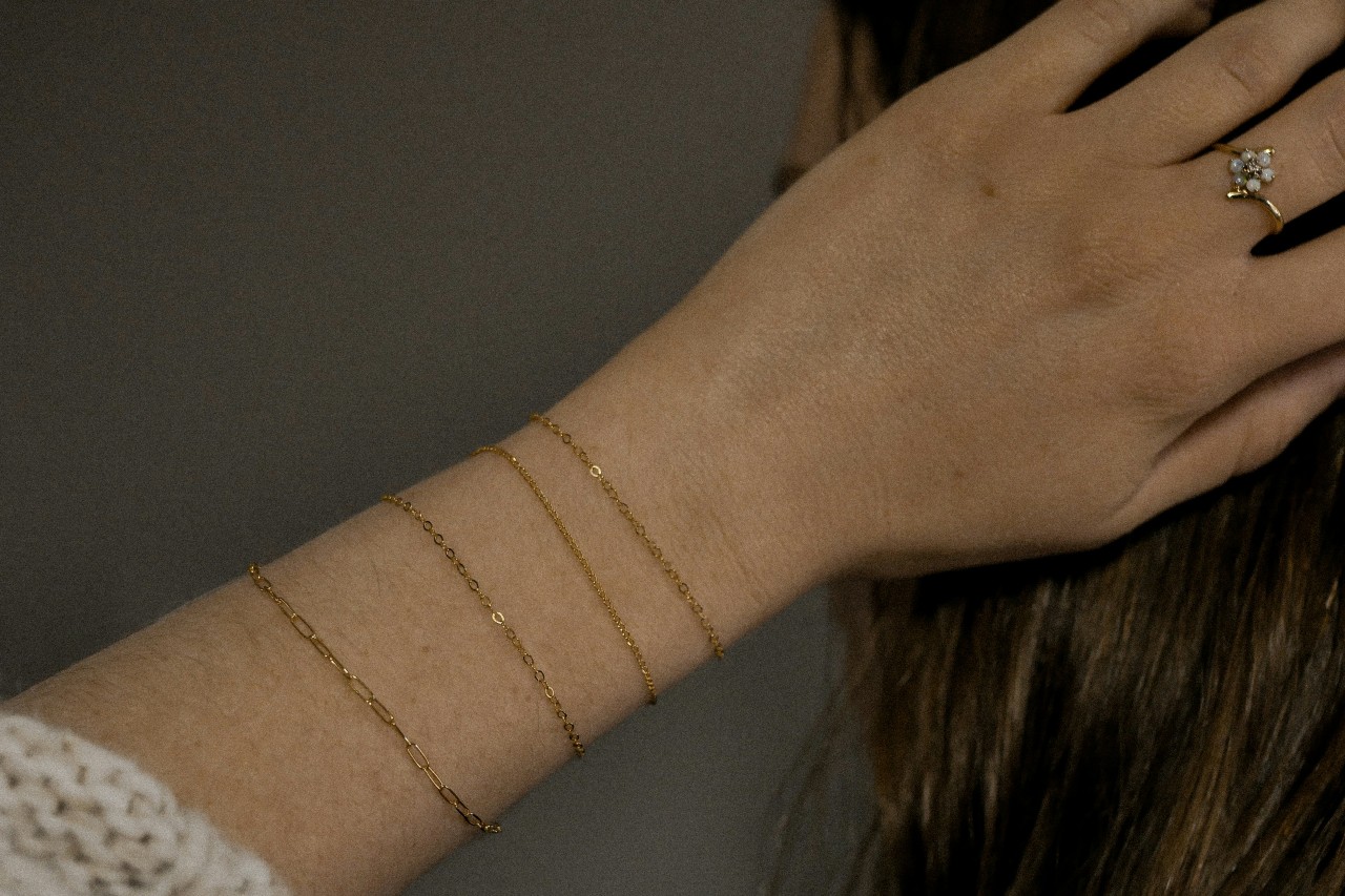 A woman with dainty yellow gold chain bracelets along with an opal halo diamond ring